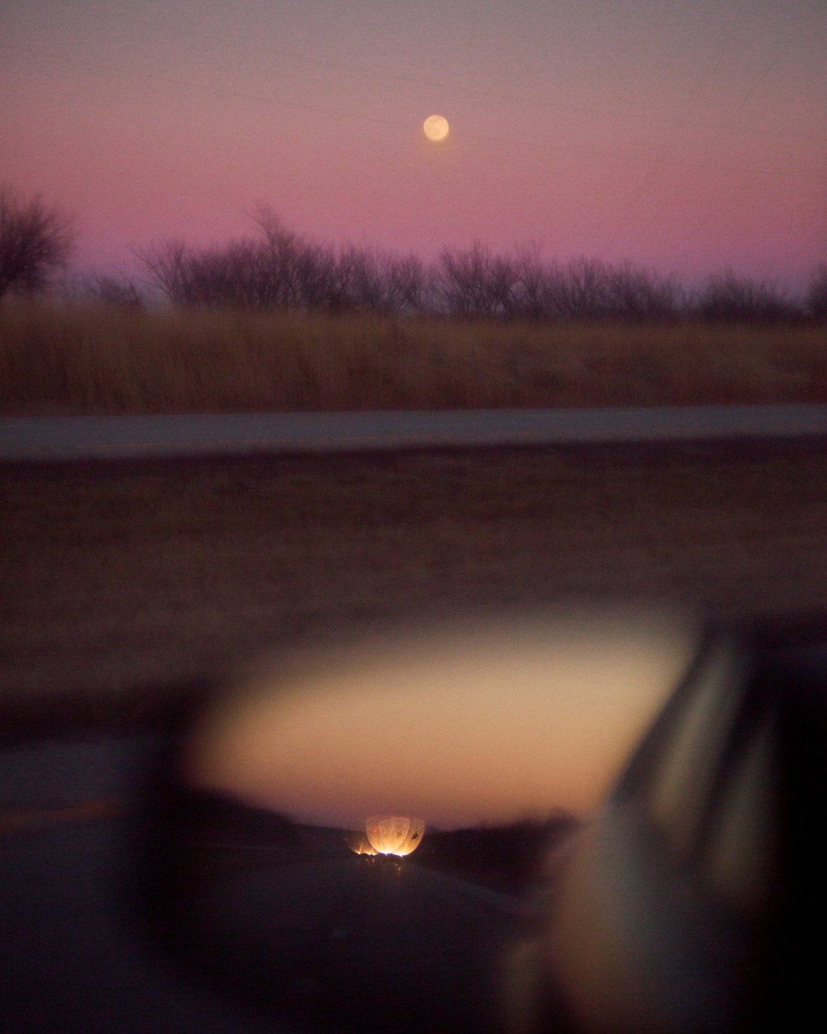A full moon over a field at dusk, seen from the road